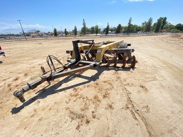 A tractor with a plow in the middle of an empty field.