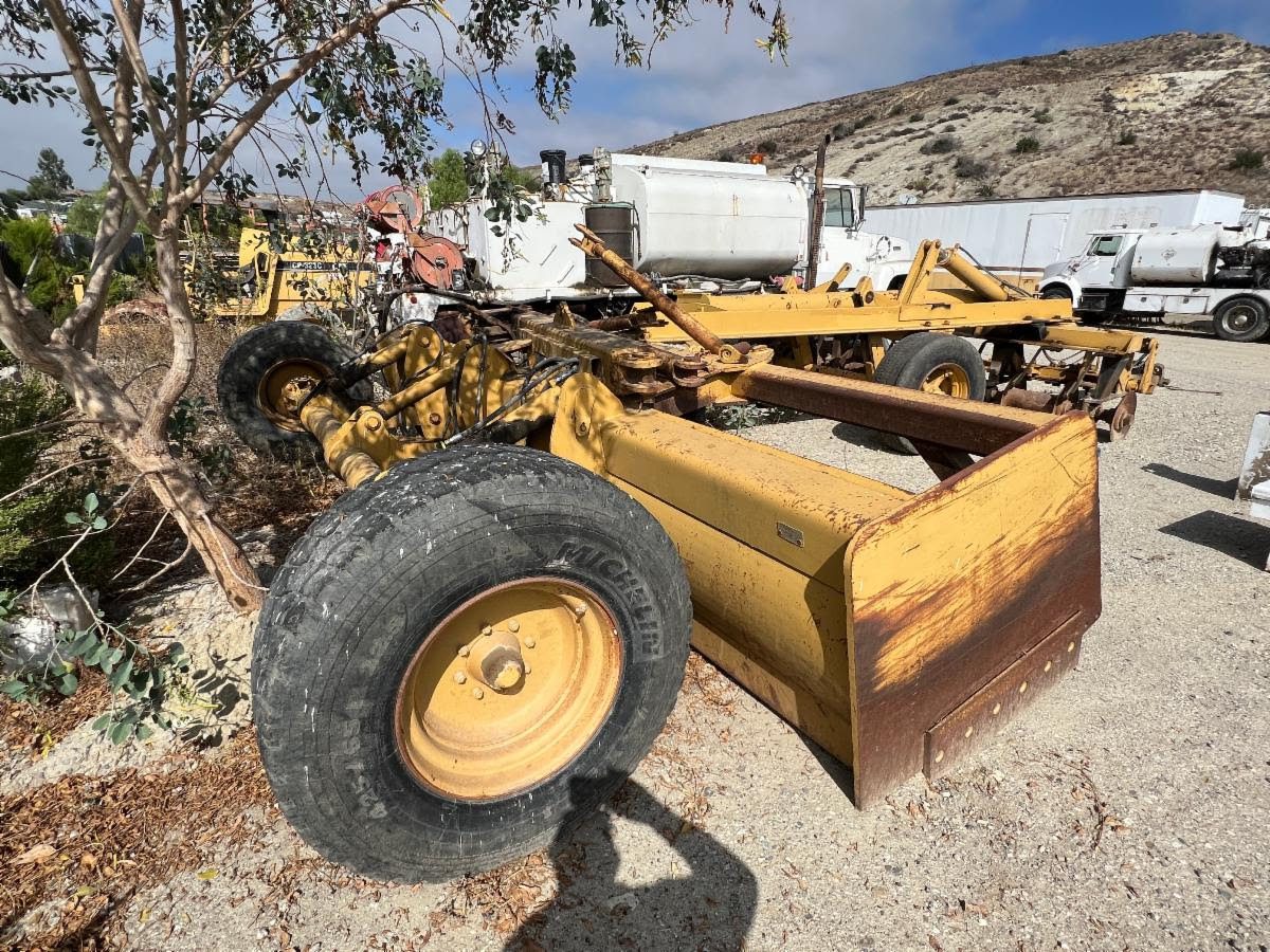 A yellow tractor sitting in the dirt next to a tree.